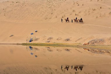 Lake Badain reflects a small tourist group starting a ride on Bactrian camels across the Badain Jaran-Badanjilin Shamo-Mysterious Lakes Desert-section of Gobi Desert. Alxa plateau-Inner Mongolia-China clipart