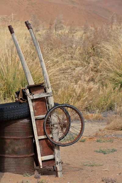 Old bike wheeled cart of rusty metal plates placed on wooden frame tied together with steel cable and rope leaning upright on oxidized oil drum. Lake Tamaying-Badain Jaran Desert-Inner Mongolia-China.