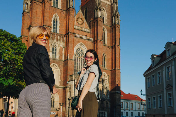 two attractive smiling women standing in front of wroclaw cathedral and looking at camera