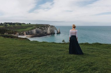back view of young woman posing on majestic cliff, Etretat, Normandy, France clipart