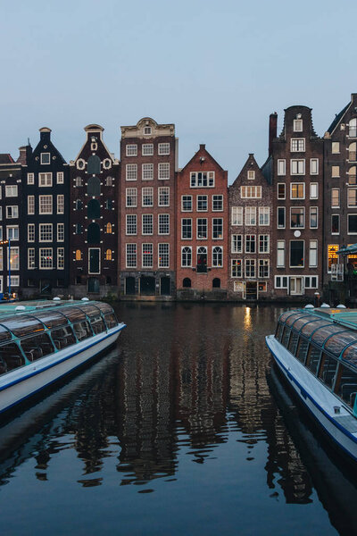 20 мая 2018 - АМСТЕРДАМ, НИДЕРЛАНДЫ: фасады древнего здания над каналом на сумерках, Амстердам, Нидерланды
