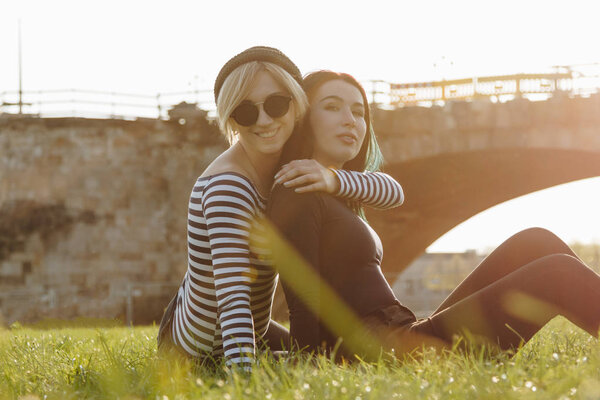 beautiful young women embracing while sitting on grass in park on sunset