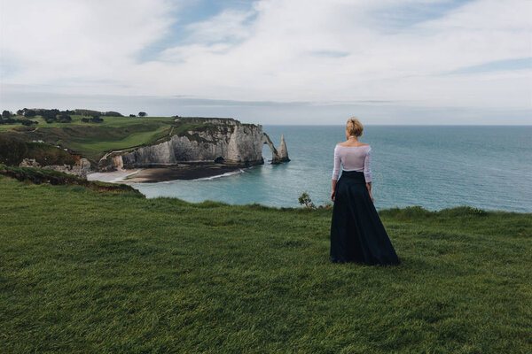 back view of young woman posing on majestic cliff, Etretat, Normandy, France
