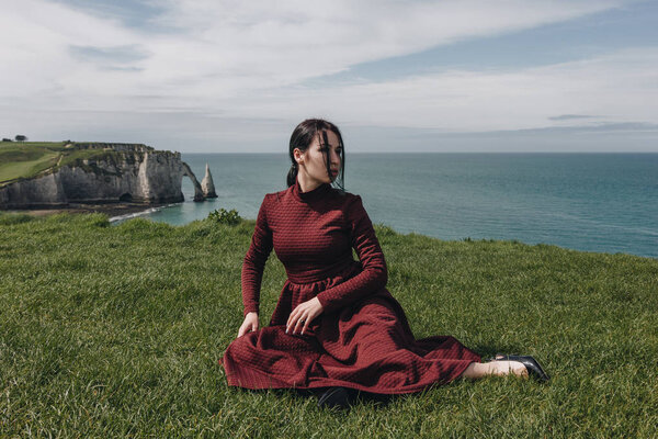 fashionable girl sitting on green cliff near the sea, Etretat, Normandy, France