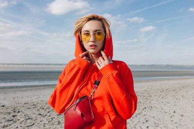 beautiful girl in red hoodie standing on beach, saint michaels mount, France clipart