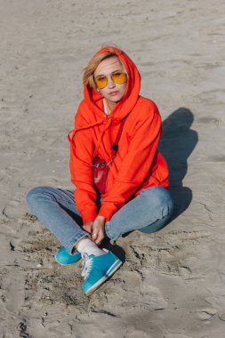 stylish girl in red hoodie sitting on sandy beach, Saint michaels mount, Normandy, France clipart