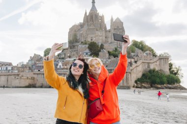 smiling tourists taking selfie on smartphone near Saint michaels mount, Normandy, France clipart