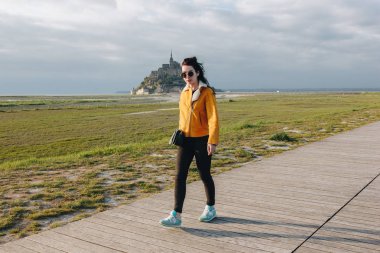 full length view of beautiful girl in sunglasses walking near mont saint michel, france clipart