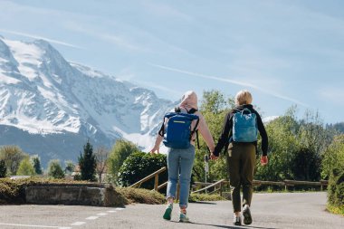 arkadan görünüşü kızlar ile el ele tutuşarak ve dağ road, mont blanc, Alpler üzerinde yürüme sırt çantaları