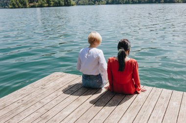 arkadan görünüşü iki genç şık kadın oturan ahşap iskele Gölü, bled, Slovenya