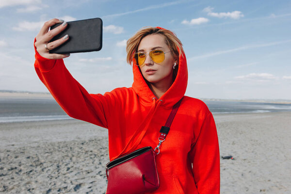 beautiful girl in red hoodie taking selfie on beach, saint michaels mount, France