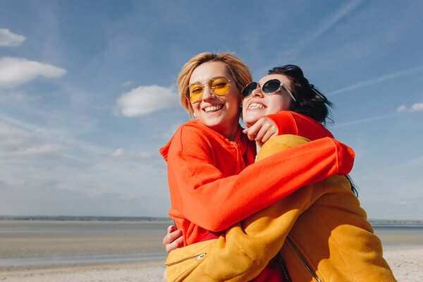 smiling female friends embracing on sandy beach, Saint michaels mount, Normandy, France