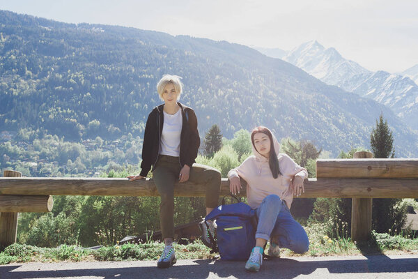 beautiful young female travelers looking at camera while resting on wooden fence in scenic mountains, mont blanc, alps