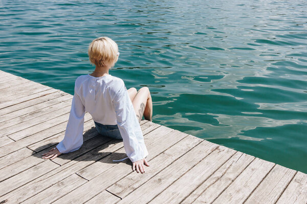 back view of stylish girl sitting on wooden pier near lake, bled, slovenia