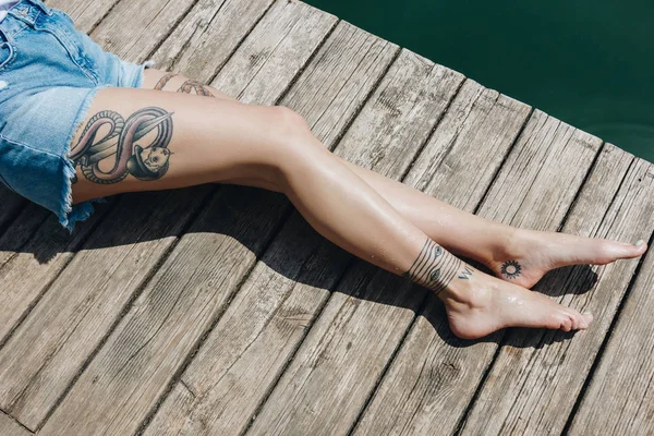 穿牛仔短裤的赤脚女孩在靠近水的木码头上被裁剪的镜头 — 图库照片