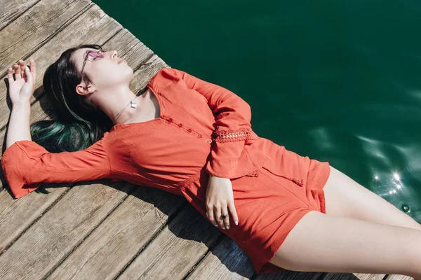 Top view of beautiful stylish girl in sunglasses lying on wooden pier near lake — Stock Image Top View Beautiful Stylish Girl Sunglasses Lying Wooden Pier Lake Royalty Free Stock Photos