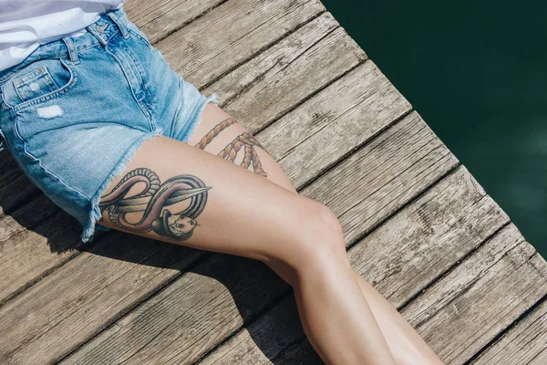 Partial top view of young woman in denim shorts resting on wooden pier near water — Stock Image Partial Top View Young Woman Denim Shorts Resting Wooden Pier Stock Picture