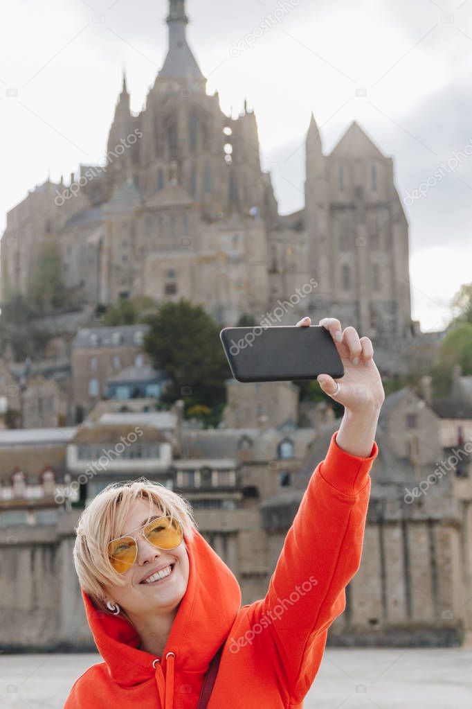 Happy girl taking selfie on smartphone near Saint michaels mount in Normandy, France