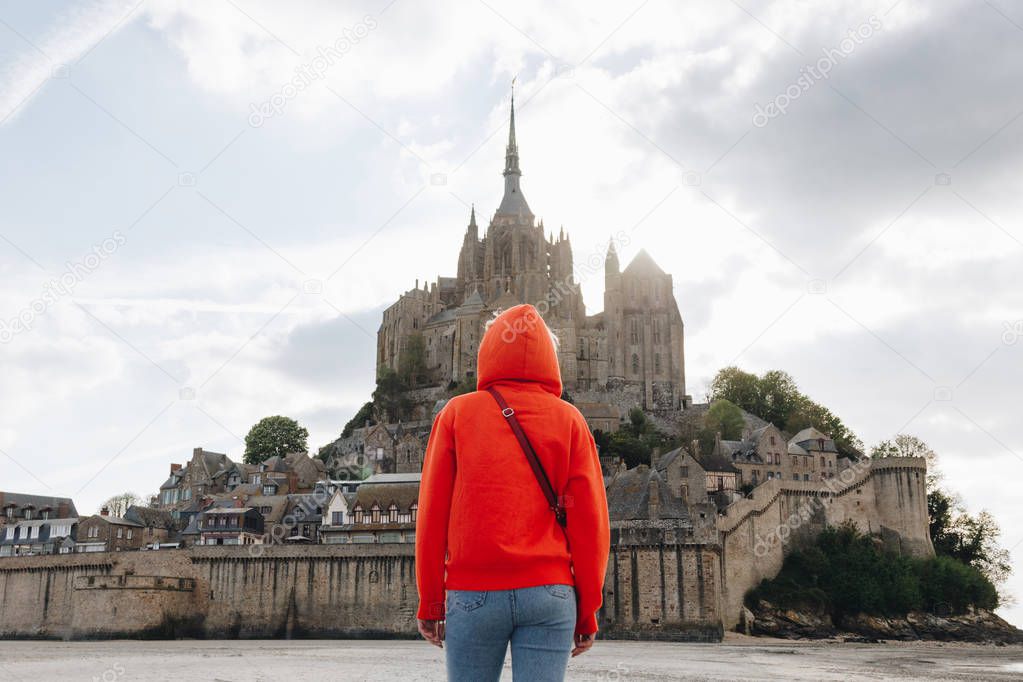 back view of girl in red looking at Saint michaels mount in Normandy, France