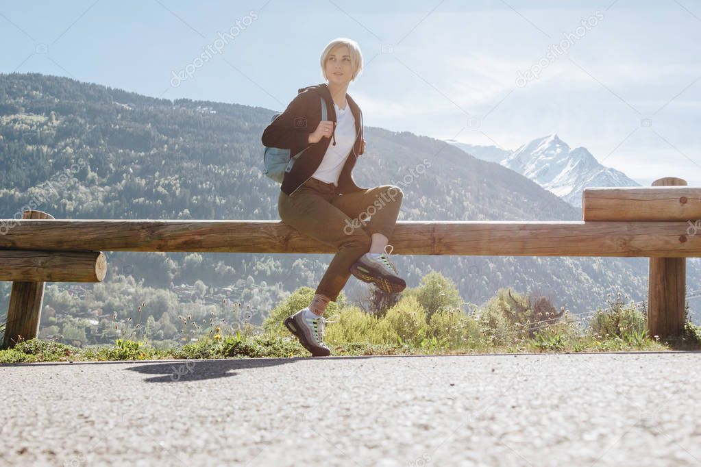 low angle view of girl with backpack sitting on wooden fence and looking away in mountains, mont blanc, alps