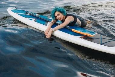sup tahta su üzerinde rahatlatıcı mavi saçlı güzel atletik dövmeli genç kadın