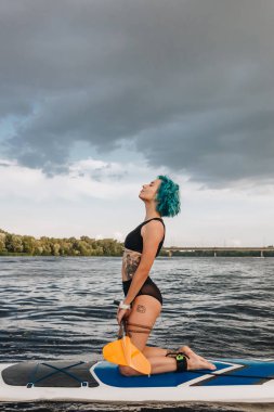 güzel atletik dövmeli kız nehirde yatılı mavi saç oynamaya