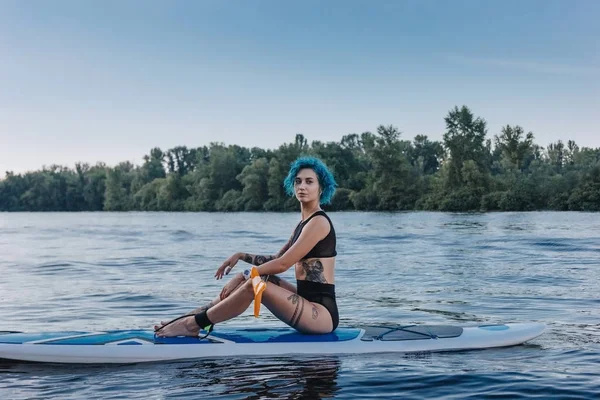 迷人的纹身运动员 蓝色的头发放松在河边板上 — 免费的图库照片