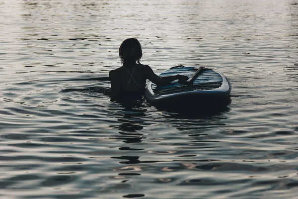 Silhouette Einer Frau Die Mit Surfbrett Wasser Schwimmt — kostenloses Stockfoto