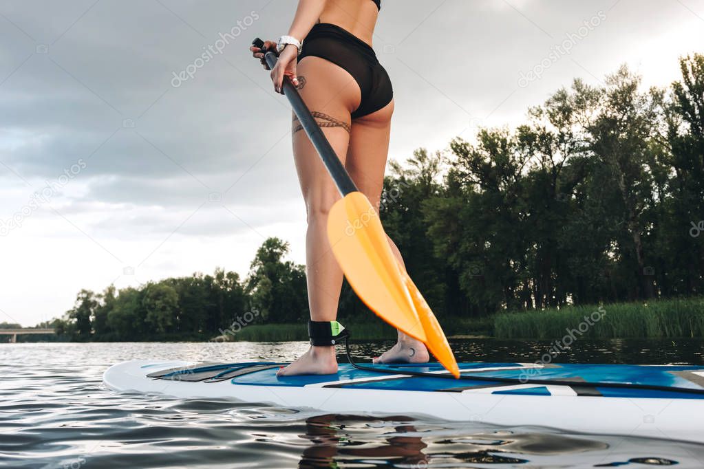 cropped view of tattooed girl standing on paddle board on water