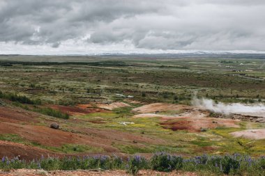 İzlanda'daki Haukadalur Vadisi'nde bulutlu gökyüzü altında volkanik bacalar, yatay, doğal görünümünü