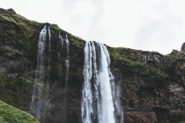 low angle view of Seljalandsfoss waterfall in highlands under cloudy sky in Iceland  clipart