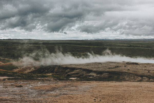 scenic view of landscape with volcanic vents under cloudy sky in Haukadalur valley in Iceland