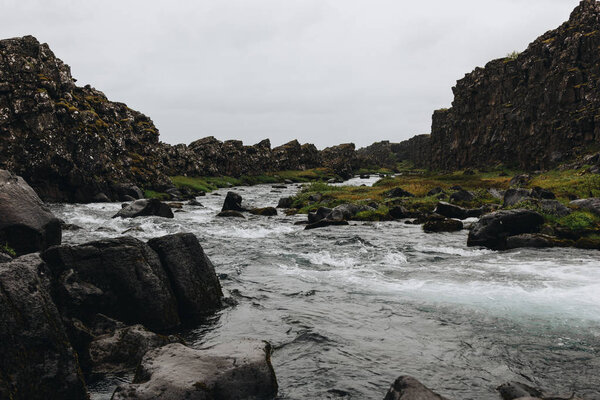 beautiful mountain river flowing through highlands under cloudy sky in Thingvellir national park in Iceland