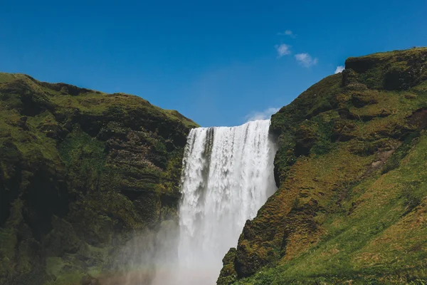 scenic view of waterfall Skogafoss against bright blue sky in Iceland