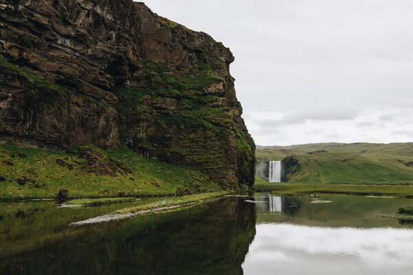 scenic view of beautiful waterfall Skogafoss in highlands under cloudy sky in Iceland 