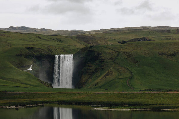 scenic view of beautiful waterfall Skogafoss in highlands under cloudy sky in Iceland 