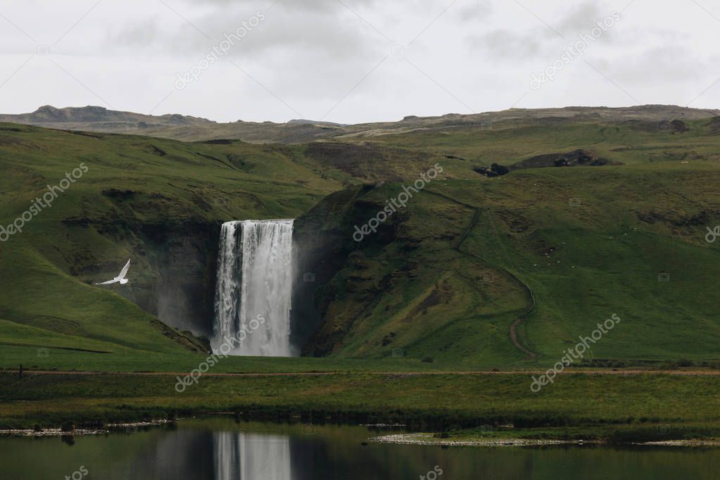 scenic view of beautiful waterfall Skogafoss in highlands under cloudy sky in Iceland 