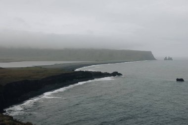 aerial view of rocky cliff and black sand beach under cloudy sky at Dyrholaey promontory in Vik, Iceland clipart