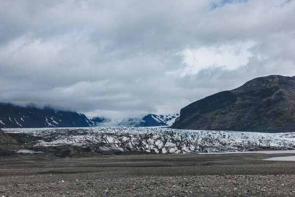 landscape with mountains covered by snow under cloudy sky in Skaftafell National Park in Iceland