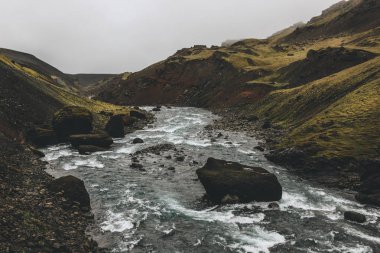 river streaming in green mountains in Iceland on misty day clipart