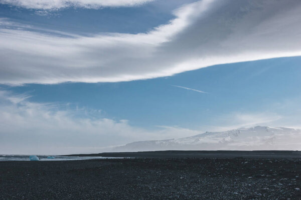 black volcanic sand on ocean coast of Jokulsarlon, Iceland under blue sky with clouds