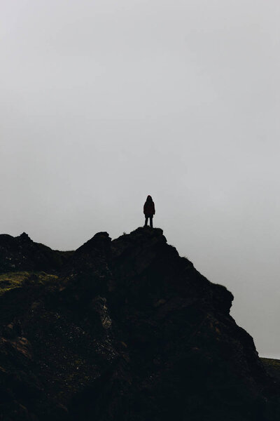 silhouette of woman standing on mountain in front of cloudy sky