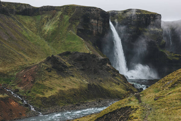 icelandic landscape with Haifoss waterfall and green hills on misty day