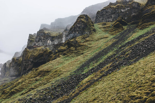 dramatic shot of mountain with green grass and rocks in Iceland on misty day