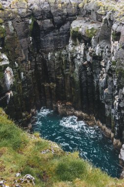 aerial view of rocky cliff and crashing blue waves in Iceland clipart