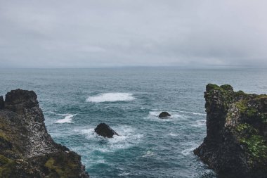 aerial view of cliffs in front of blue ocean in Arnarstapi, Iceland on cloudy day clipart