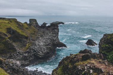 scenic view of beautiful cliffs in front of blue ocean in Arnarstapi, Iceland on cloudy day clipart