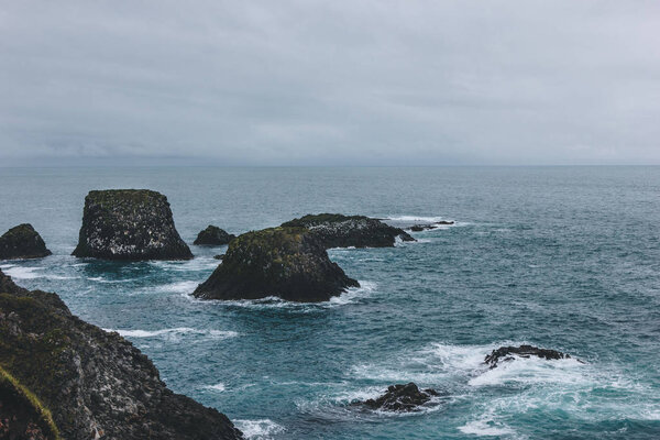 dramatic shot of rocks in blue ocean in Arnarstapi, Iceland on cloudy day