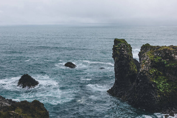 rocky cliffs in front of blue ocean in Arnarstapi, Iceland on cloudy day