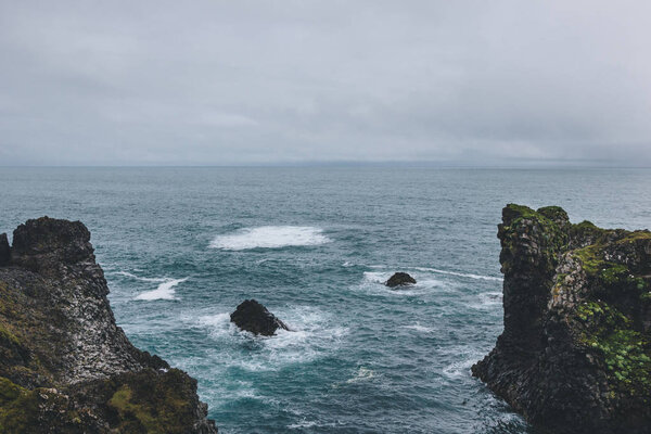 aerial view of cliffs in front of blue ocean in Arnarstapi, Iceland on cloudy day